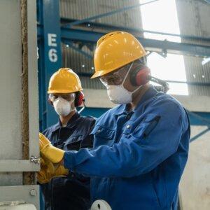 Two workers wearing hearing protection, hard hats, and face masks