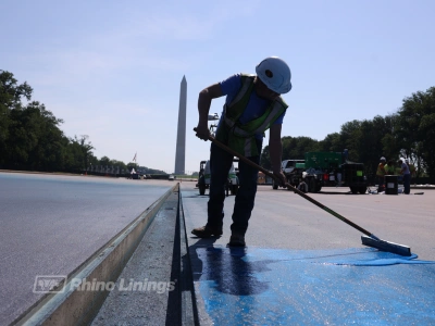 close up of contractor spreading blue epoxy protective coating on reflecting pool concrete