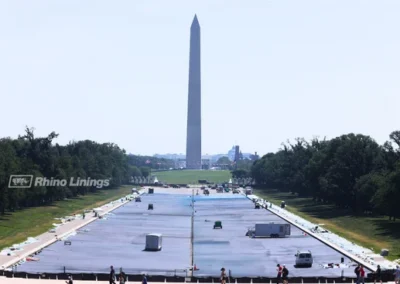 wide-angle-view-of-reflecting-pool-with-contractors-working-on-waterproofing-monument-in-background